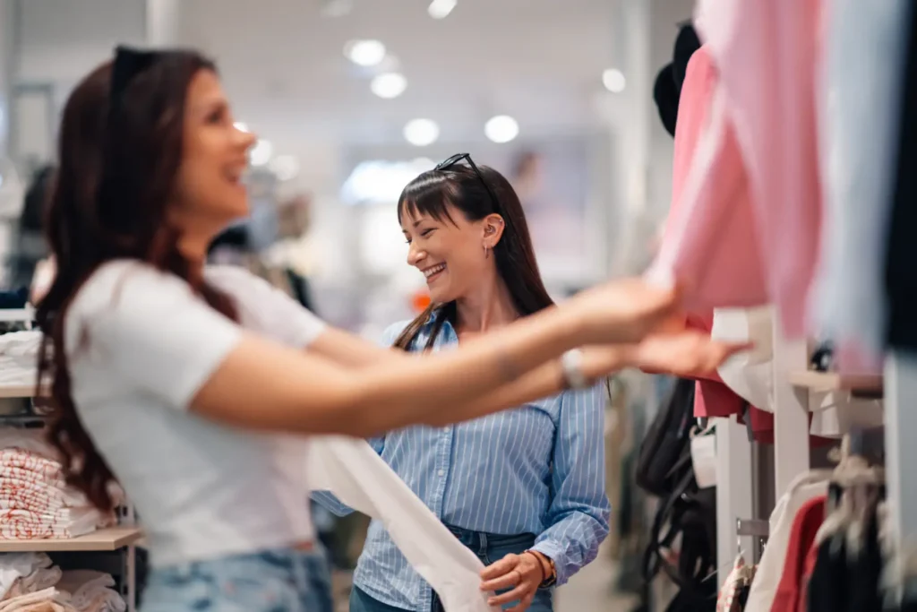 Two women smiling while looking at clothing.